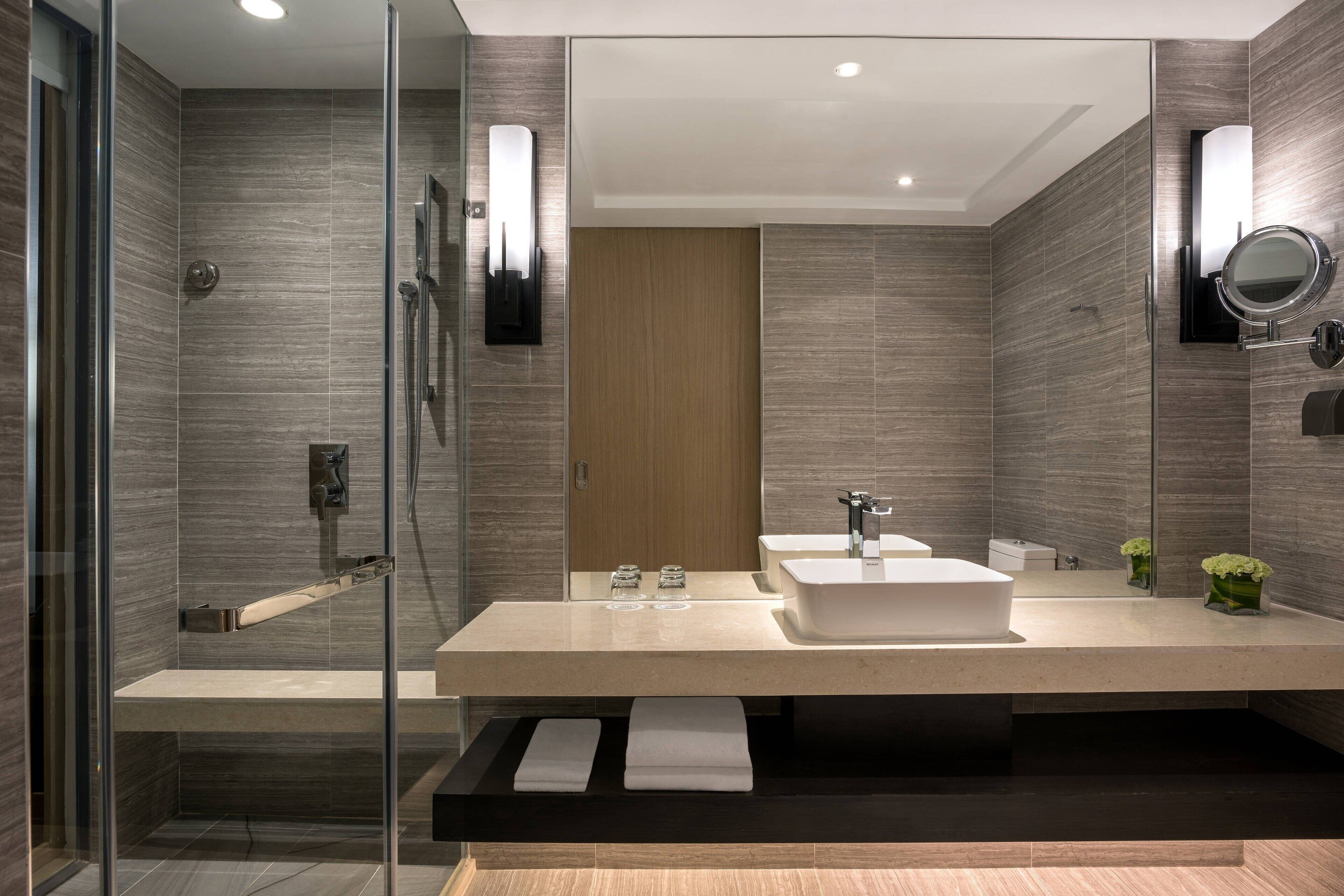 A modern bathroom with a glass-enclosed shower, a large vanity with a sink, and a mirror.