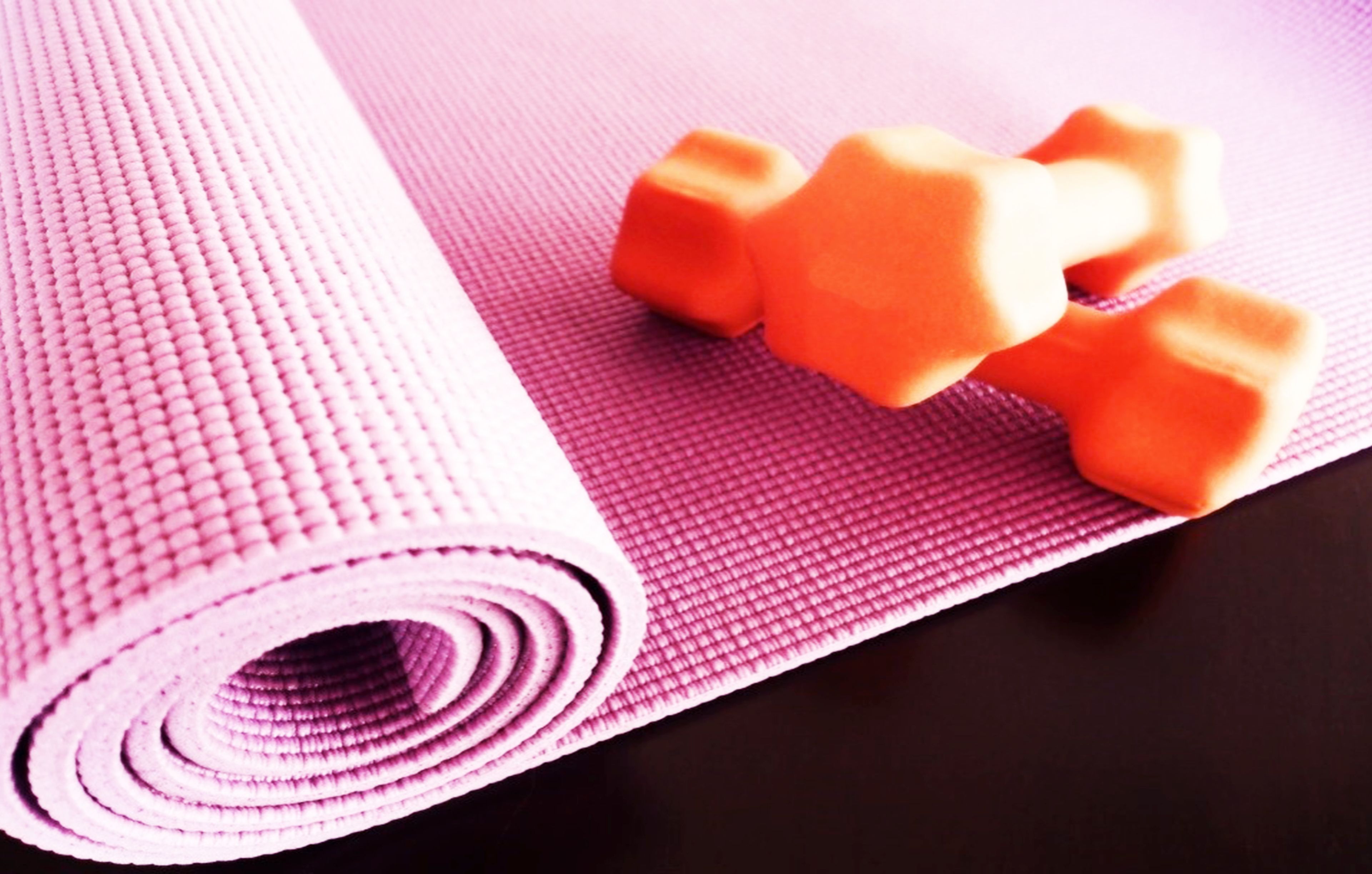 A pink yoga mat with two orange dumbbells on it.