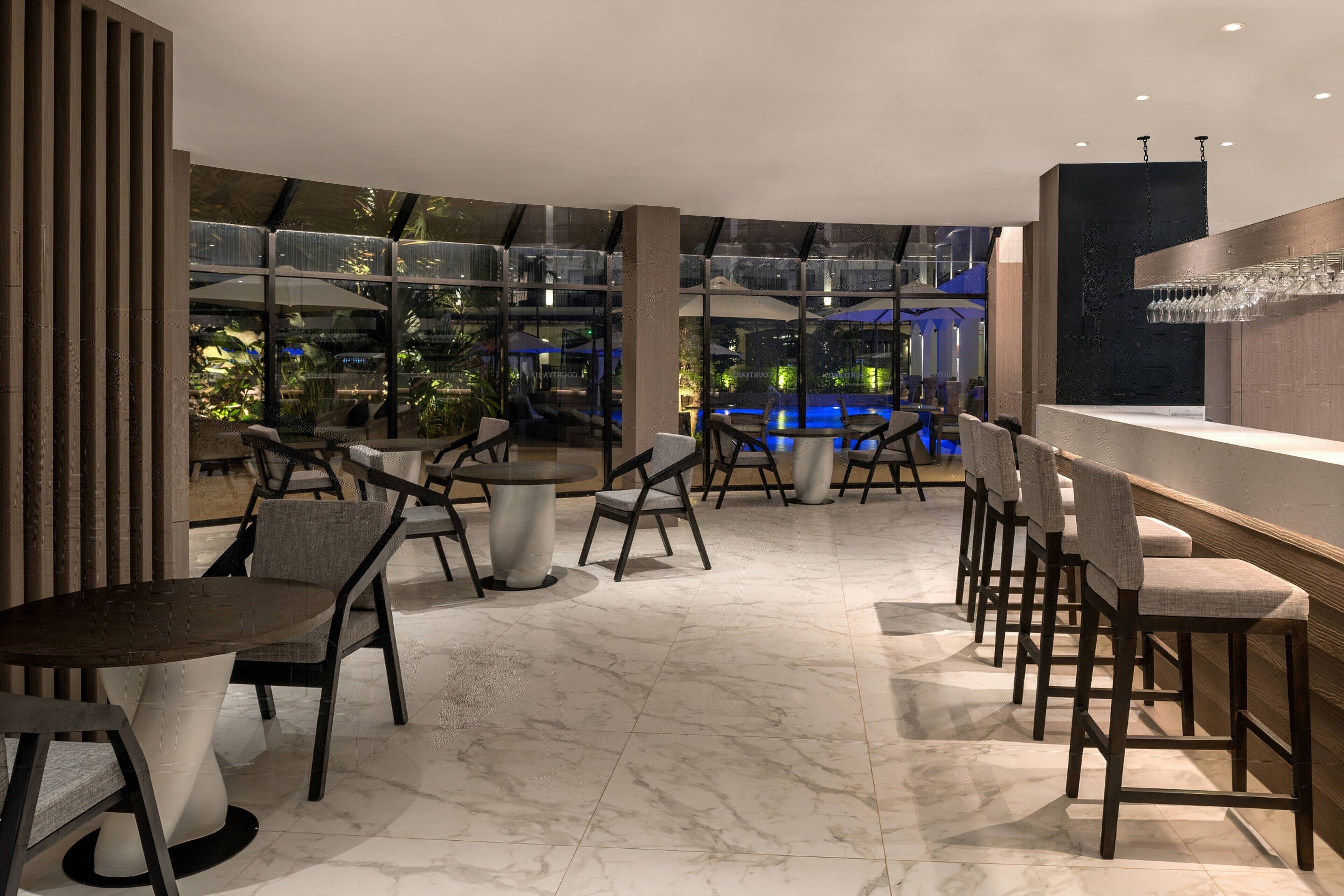 A modern indoor space with a bar area, seating arrangements, and a view of an outdoor pool area.