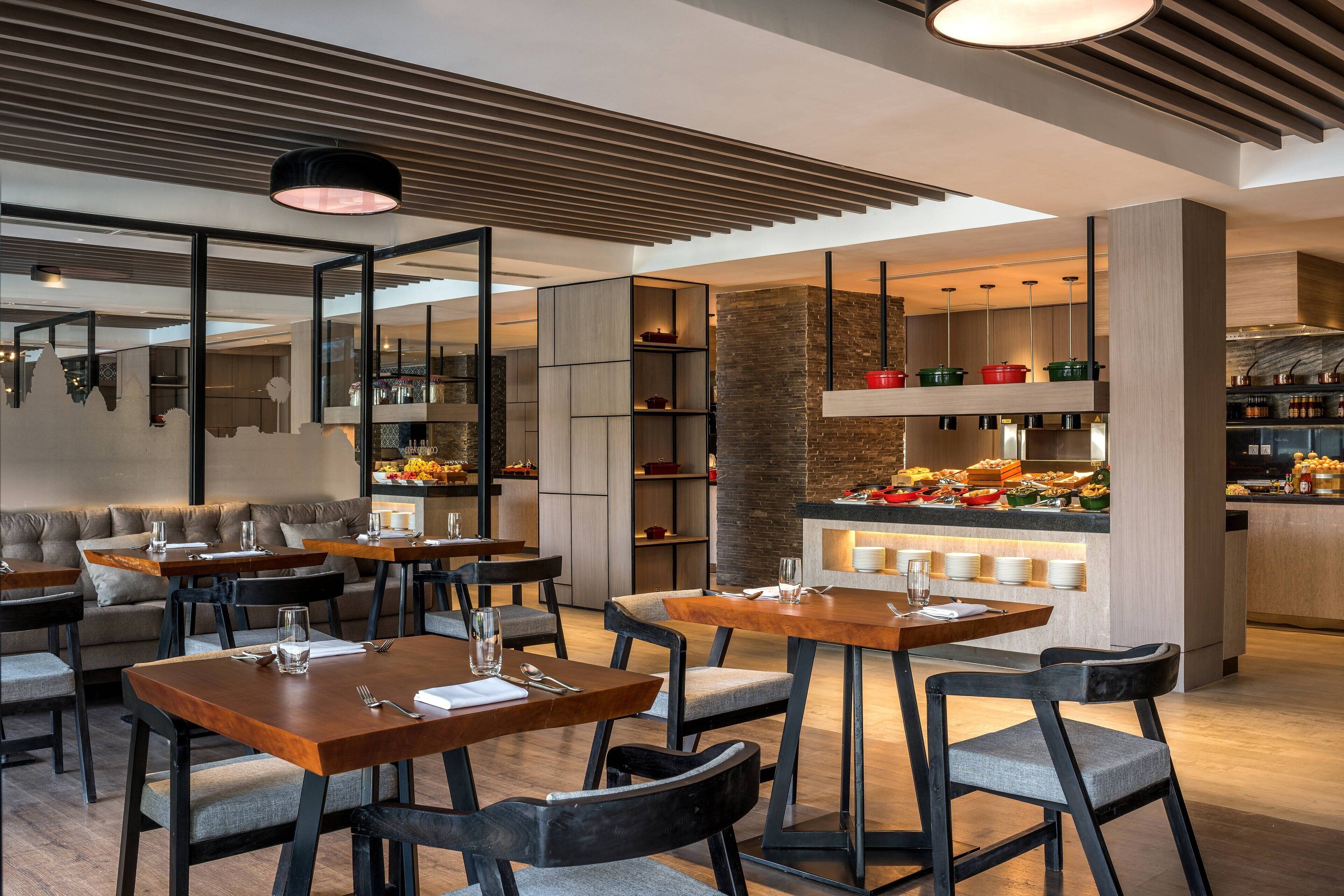 Ein moderner Essbereich mit Holztischen und -stühlen, eine Küchenzeile mit einem Buffet und eine Sitzecke mit einer Couch und Sesseln.