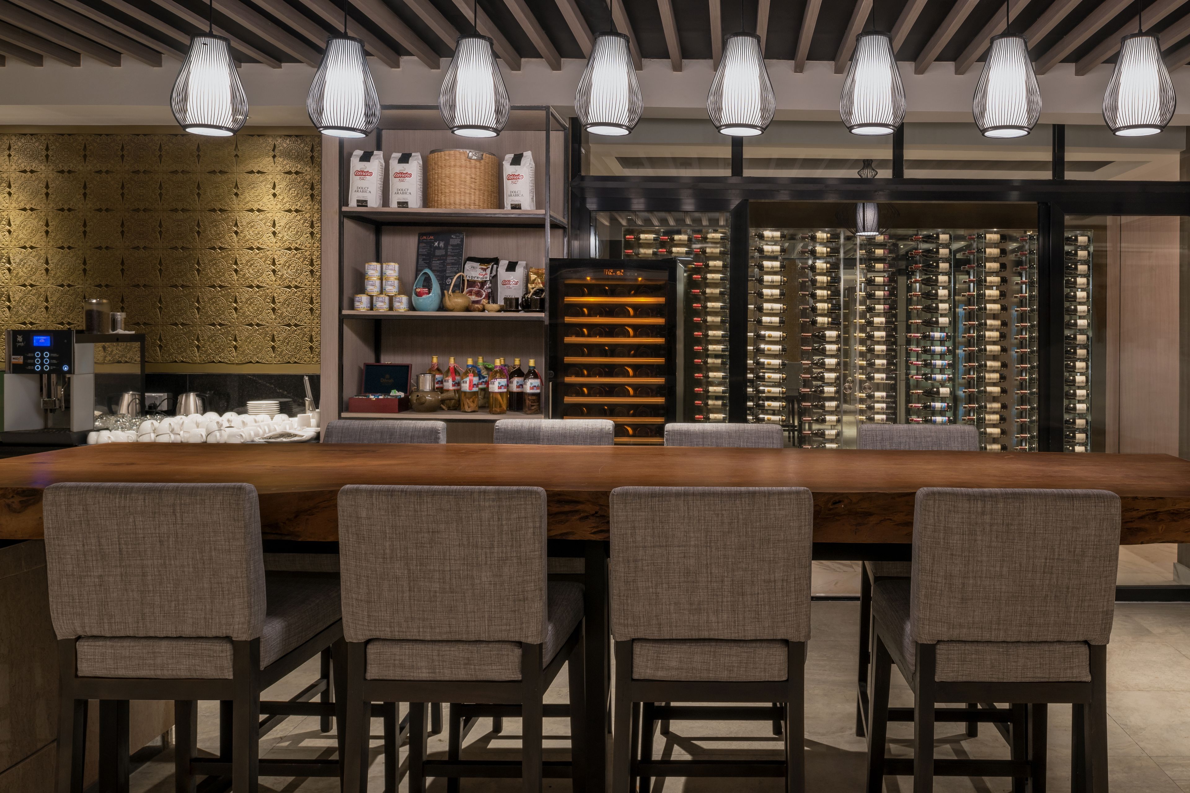 A modern bar area with a long wooden counter, multiple seating options, and a wine rack.