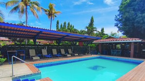 Une piscine avec un bord carrelé, des chaises longues et un espace de repos abrité.
