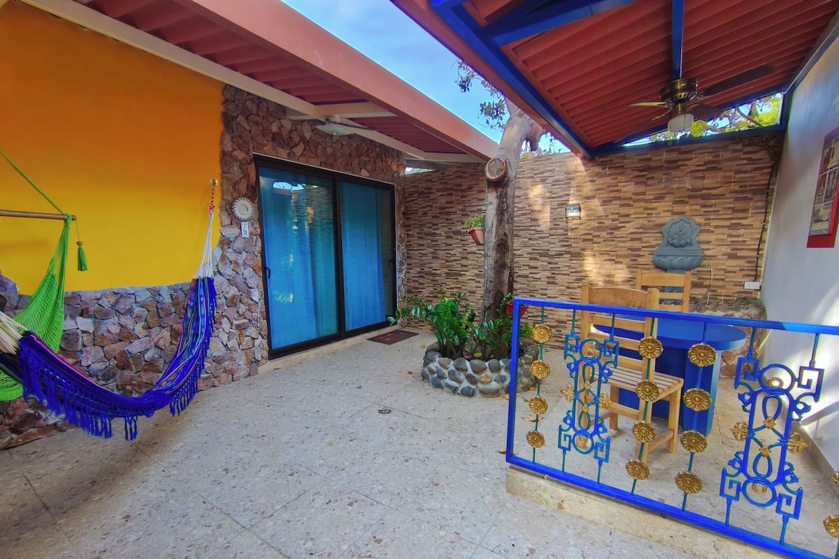 Un espace extérieur abrité, doté d’un mur en pierre, d’un hamac, d’une porte bleue et d’une rambarde bleue agrémentée d’éléments décoratifs.