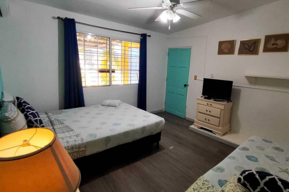 Une chambre à coucher avec un lit, une table de chevet, un téléviseur et une fenêtre avec des rideaux.