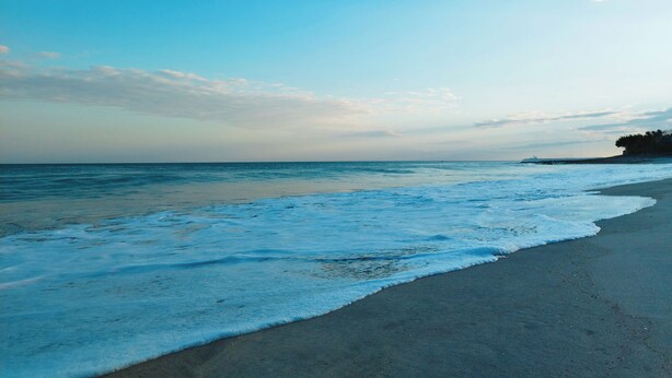 Een strand met heldere lucht en rustige golven.