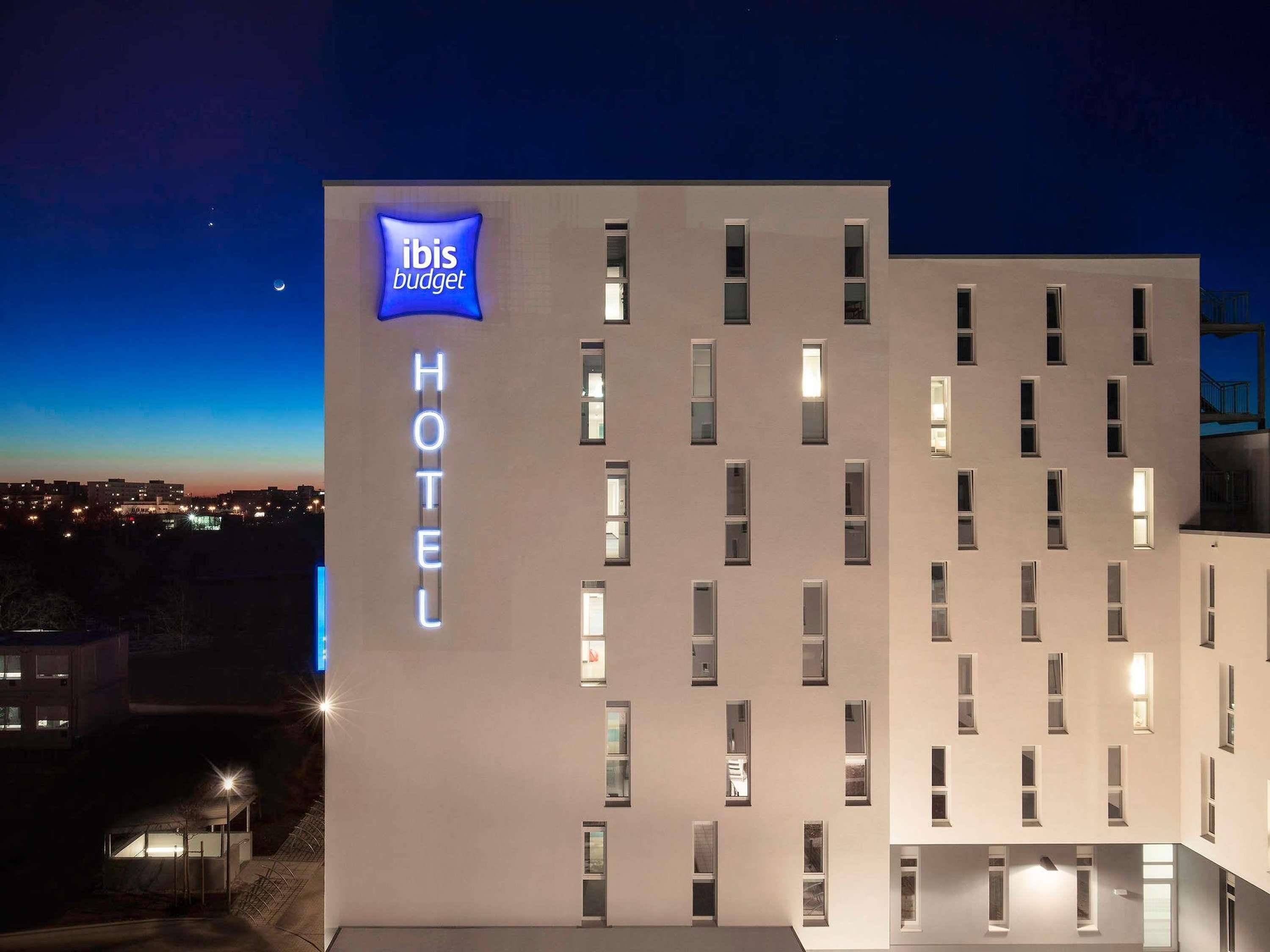 A modern hotel building with a prominent 'ibis budget' sign, multiple windows, and a flat facade.