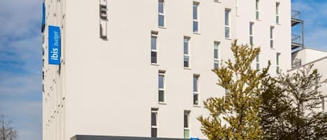 Ein modernes Hotelgebäude mit einem gut sichtbaren 'ibis budget'-Schild, zahlreichen Fenstern und einer glatten Fassade.