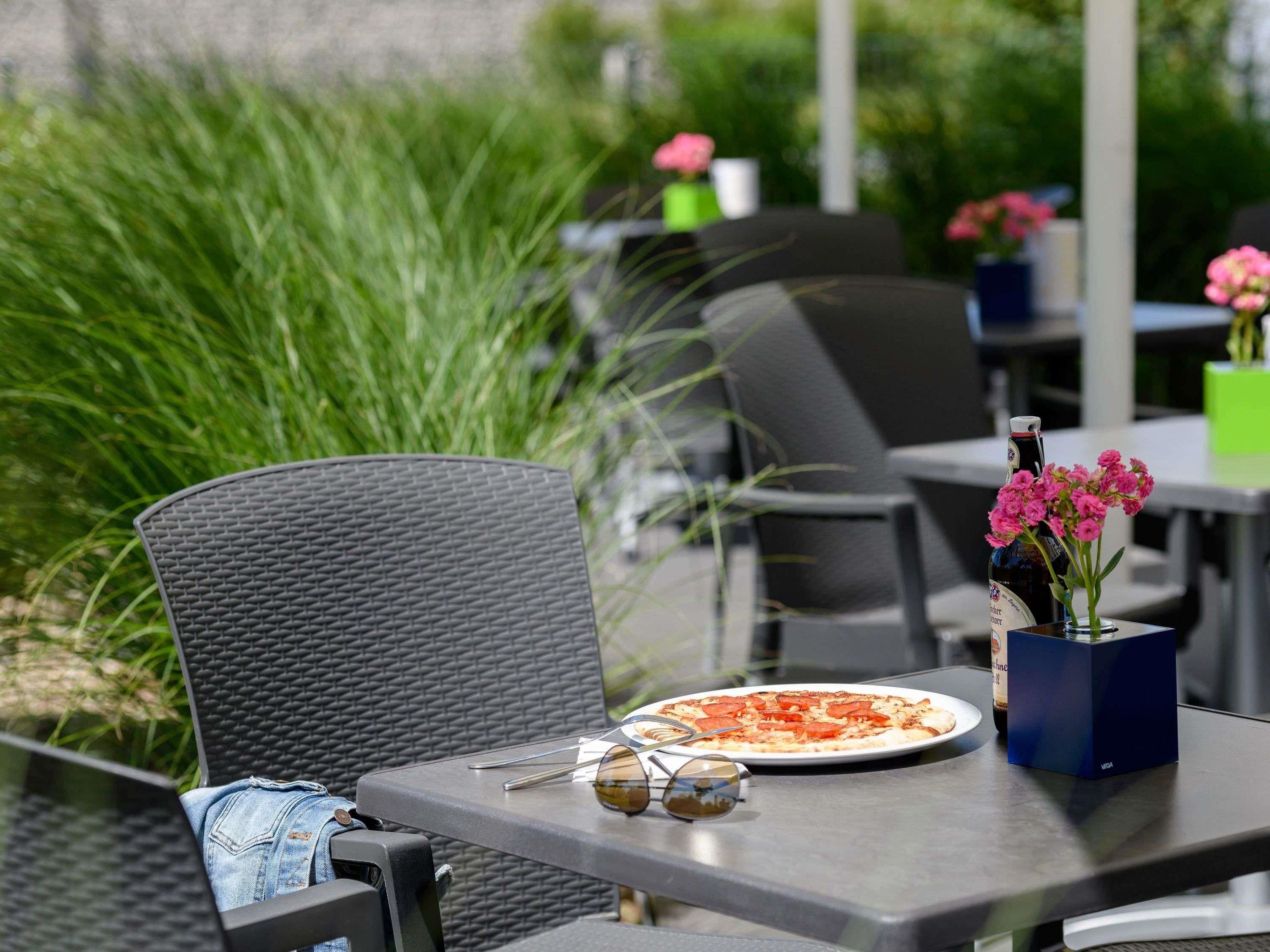 An outdoor dining area with a table, chairs, a pizza, a bottle, and a vase with flowers.