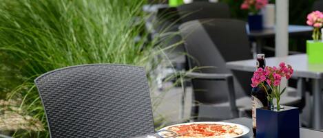 An outdoor dining area with a table, chairs, a pizza, a bottle, and a vase with flowers.