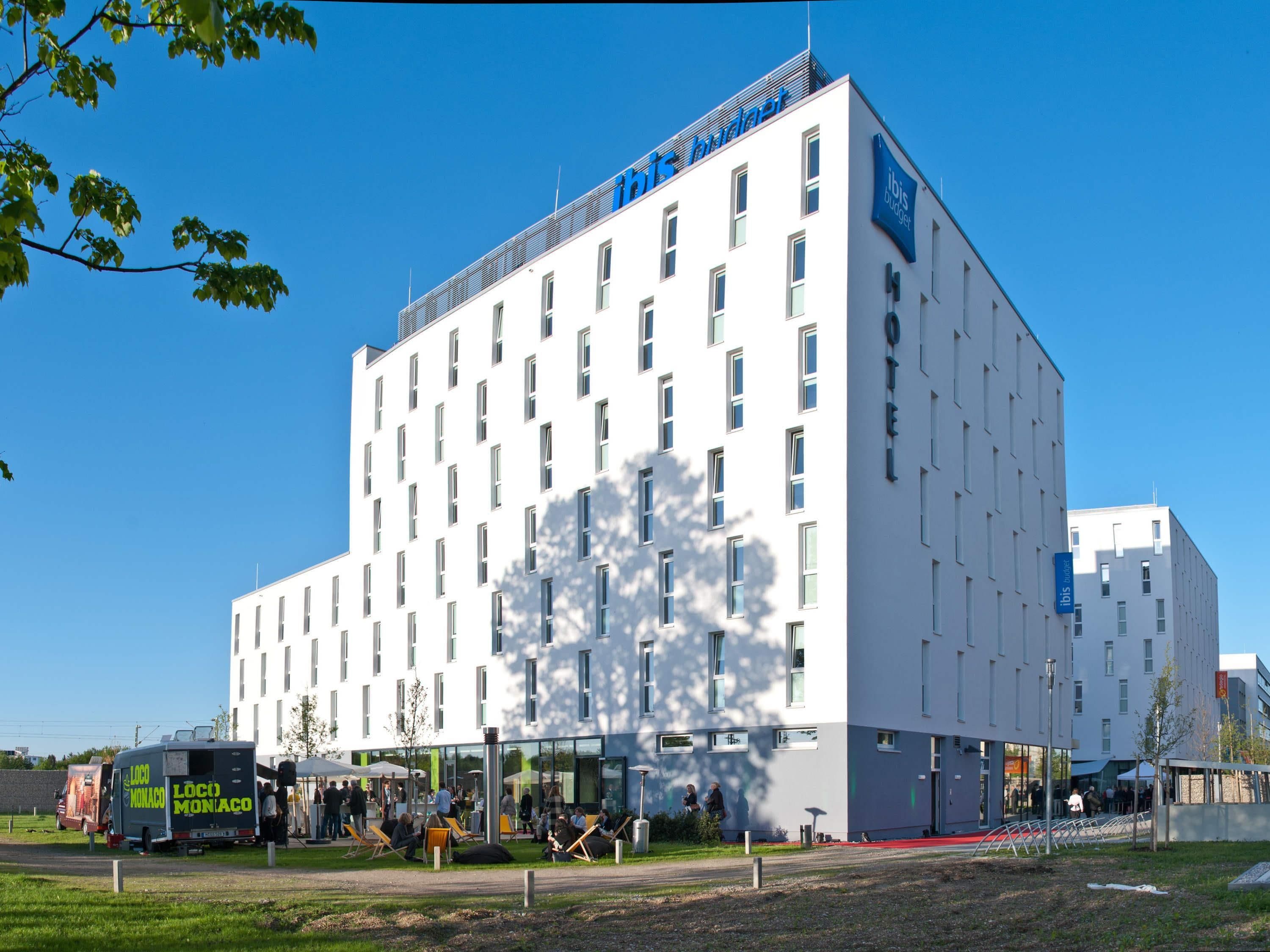 A modern hotel with a white facade, multiple windows, and a sign indicating it is part of the ibis budget hotel chain.