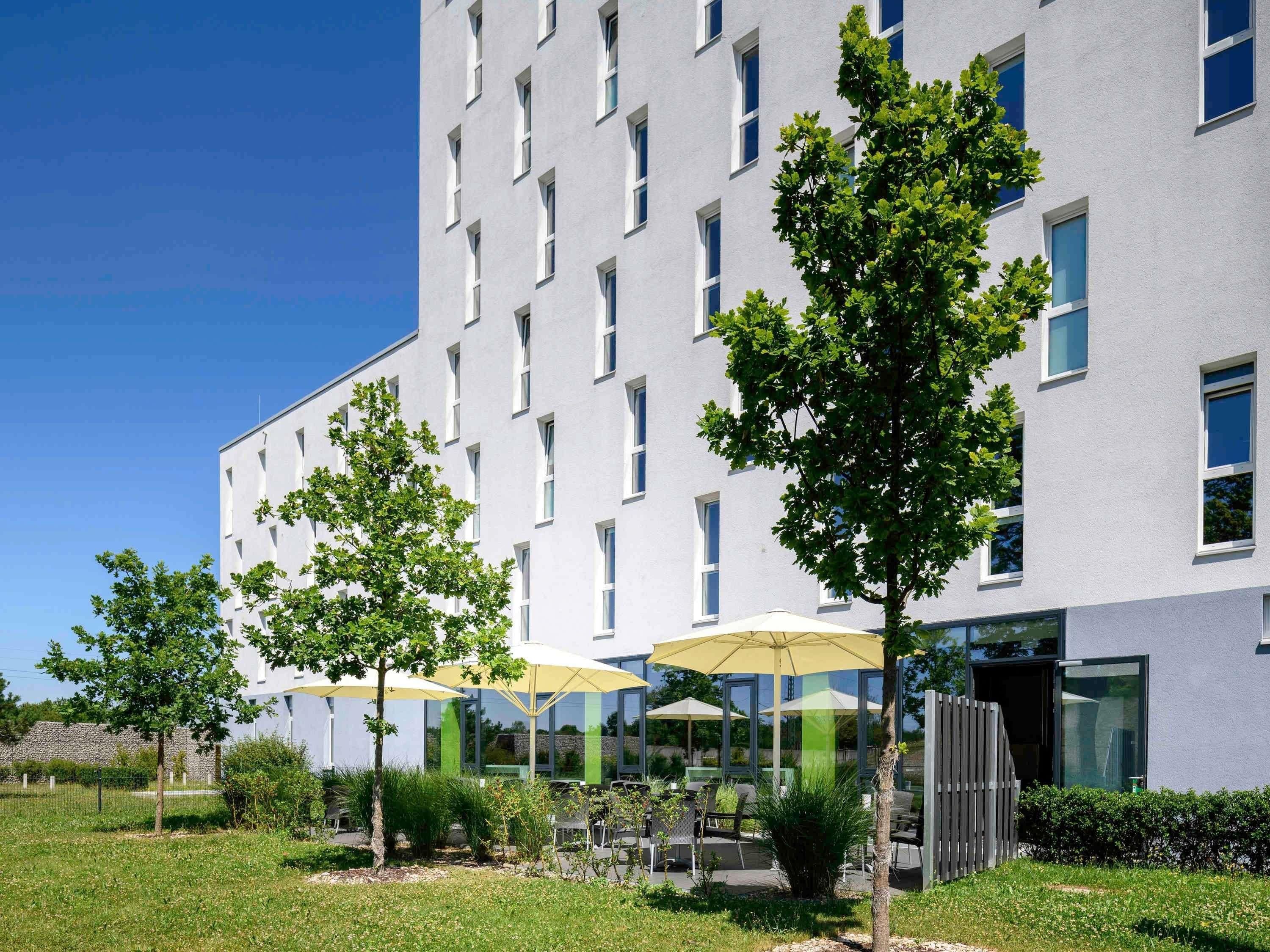 Um edif ício moderno com fachada plana, várias janelas e área de estar externa com guarda-sóis.
