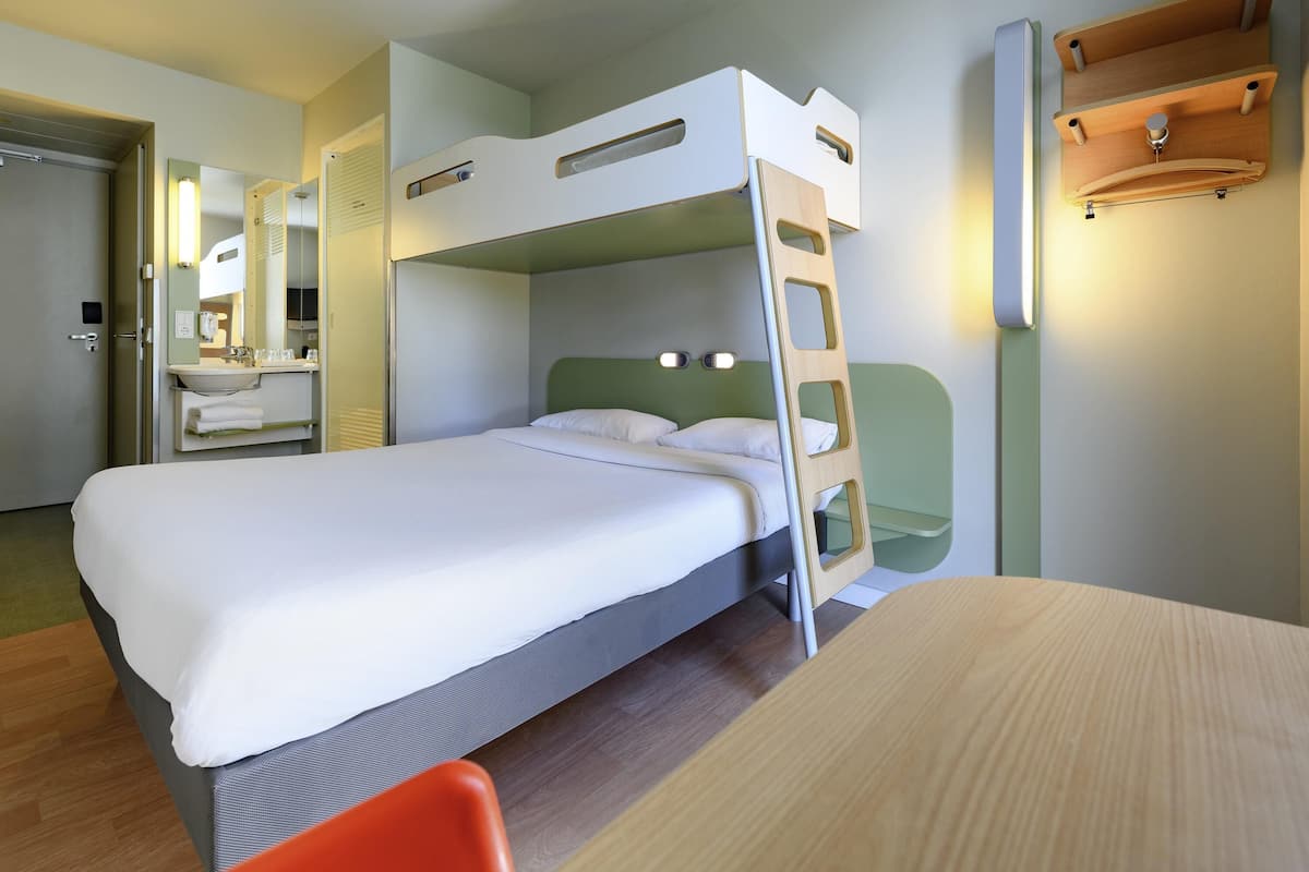 Un lit superposé avec une échelle, une table de chevet, un miroir et une étagère fixée au mur.