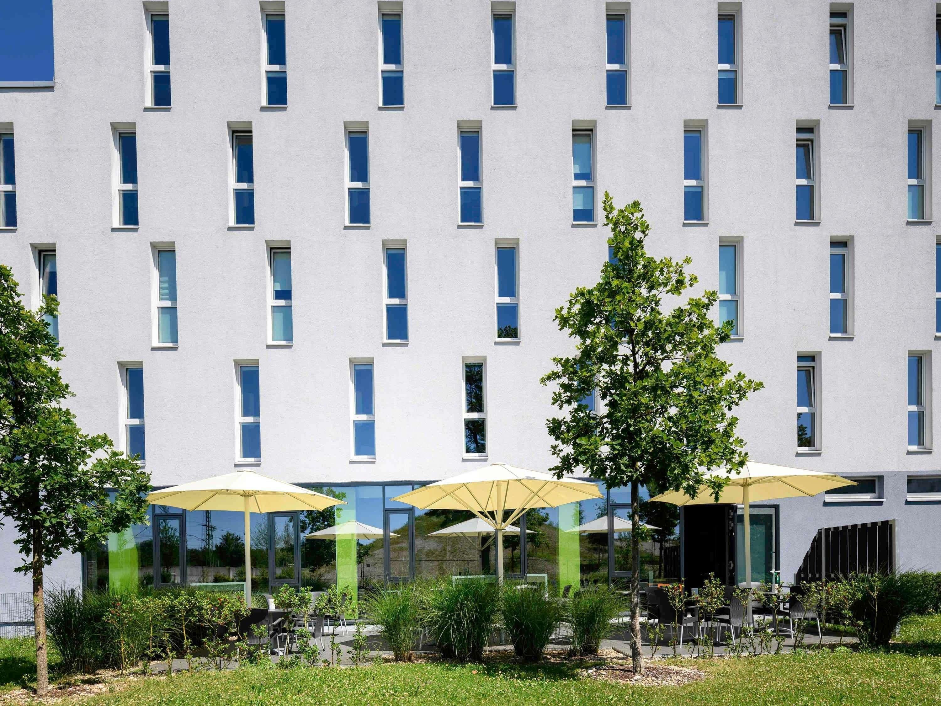 Un edificio moderno con una hilera de ventanas y mesas al aire libre con sombrillas.