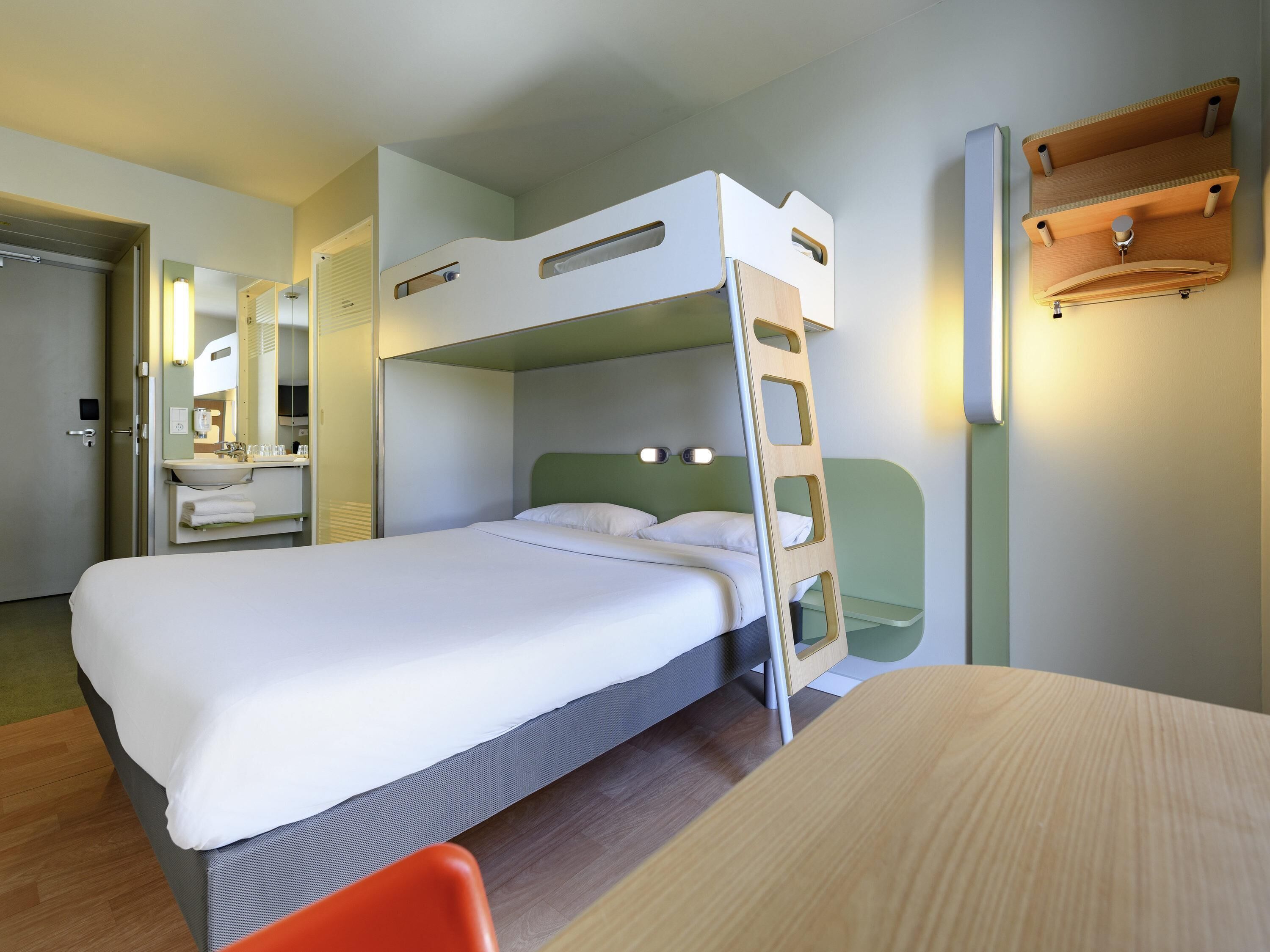 Un lit superposé avec une échelle, une table de chevet, un miroir et une étagère fixée au mur.