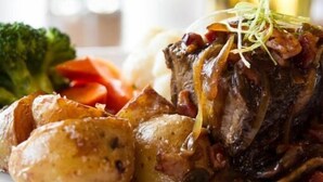 A plate with roasted meat, potatoes, and vegetables, accompanied by a glass of beer. - The Lodge at Arrow Lakes (Nakusp)