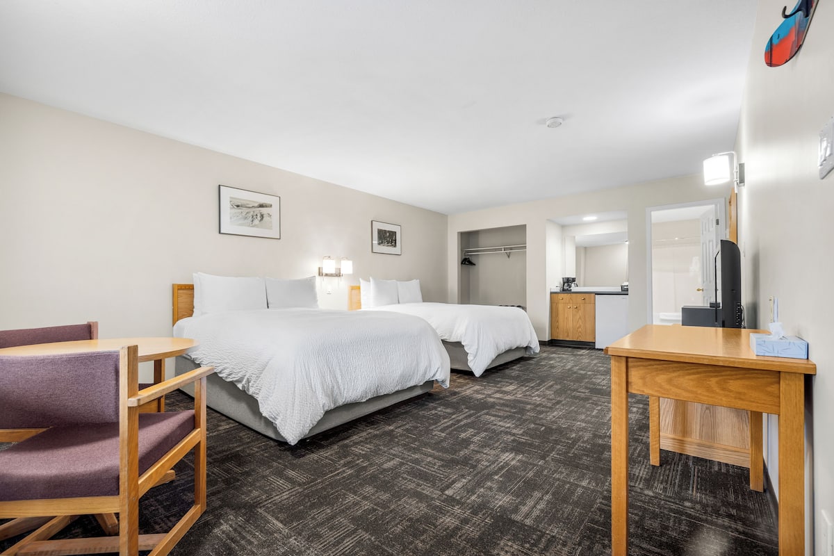 Ein Hotelzimmer mit zwei Betten, einem Schreibtisch, einem Stuhl, einem Kleiderschrank und einem durch eine offene Tür einsehbaren Badezimmer.