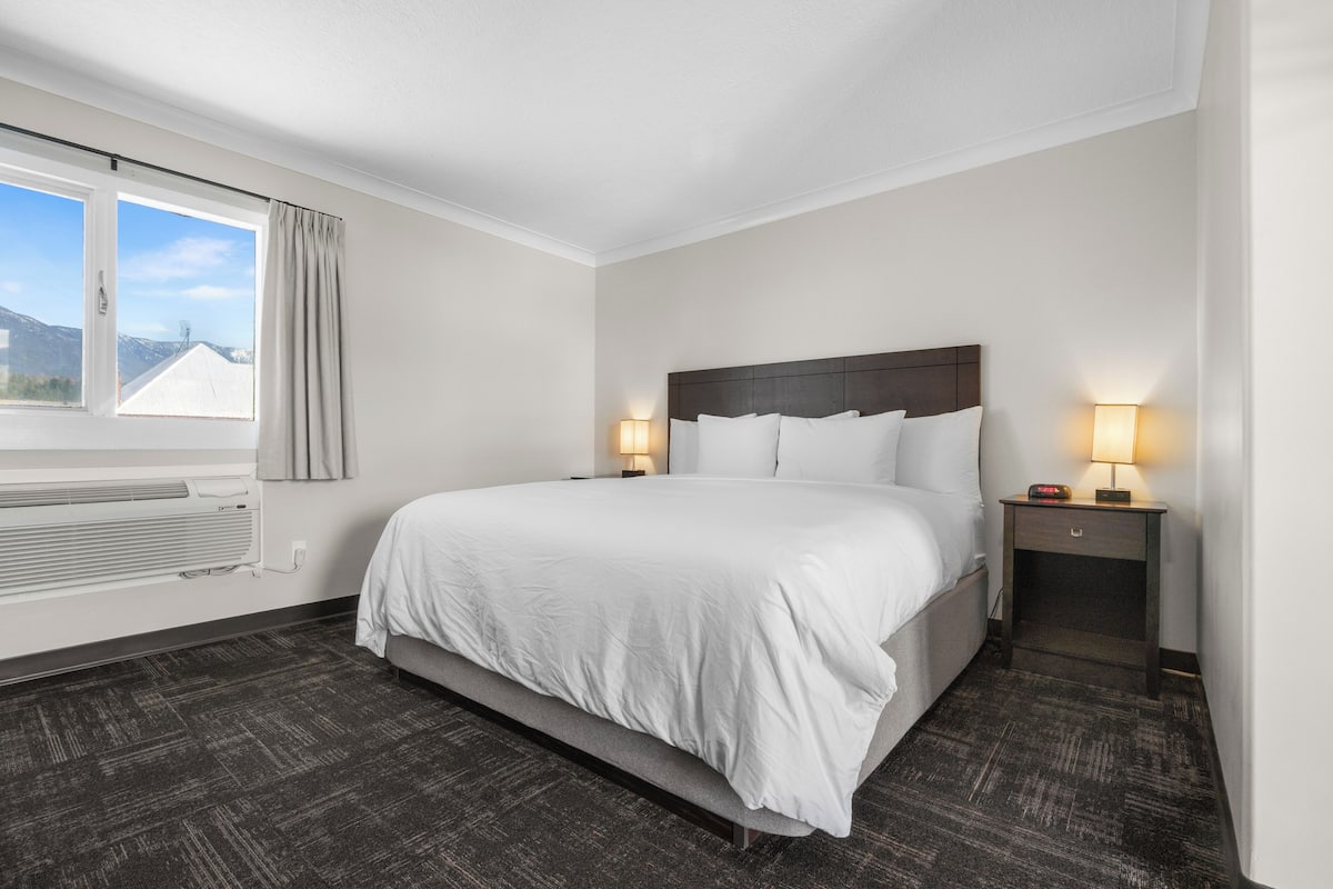 Ein Hotelzimmer mit einem großen Bett, zwei Nachttischen mit Lampen, einem Fenster mit Vorhängen und einem Heizkörper.