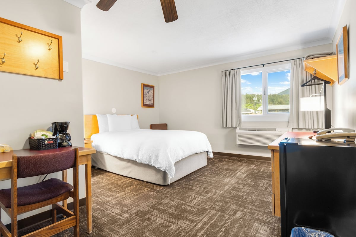 Ein Hotelzimmer mit Bett, Schreibtisch, Stuhl und einem Vorhangfenster.