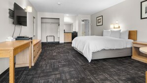 A hotel room with a bed, bedside tables, a desk, a flat-screen TV, a wardrobe, and a bathroom door. - The Lodge at Arrow Lakes (Nakusp)