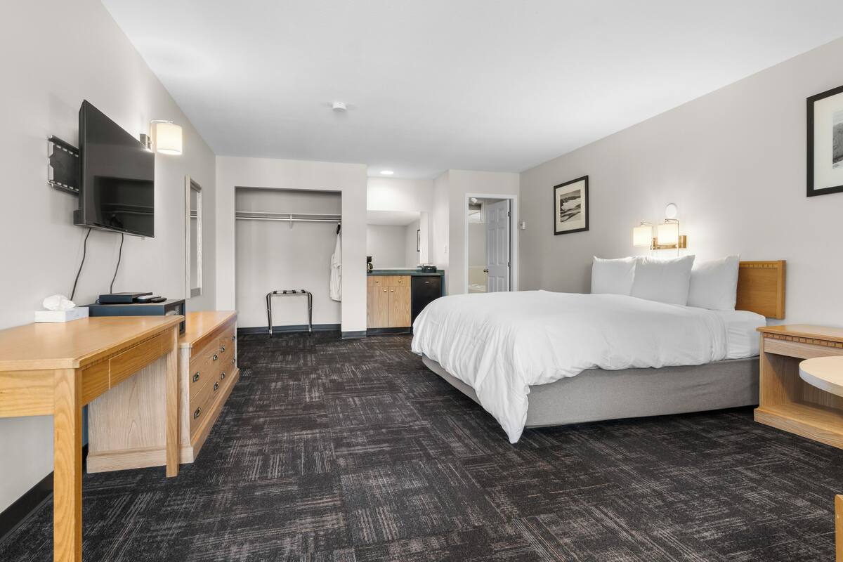 Ein Hotelzimmer mit Bett, Nachttischen, Schreibtisch, Flachbildfernseher, Kleiderschrank und Badezimmertür.