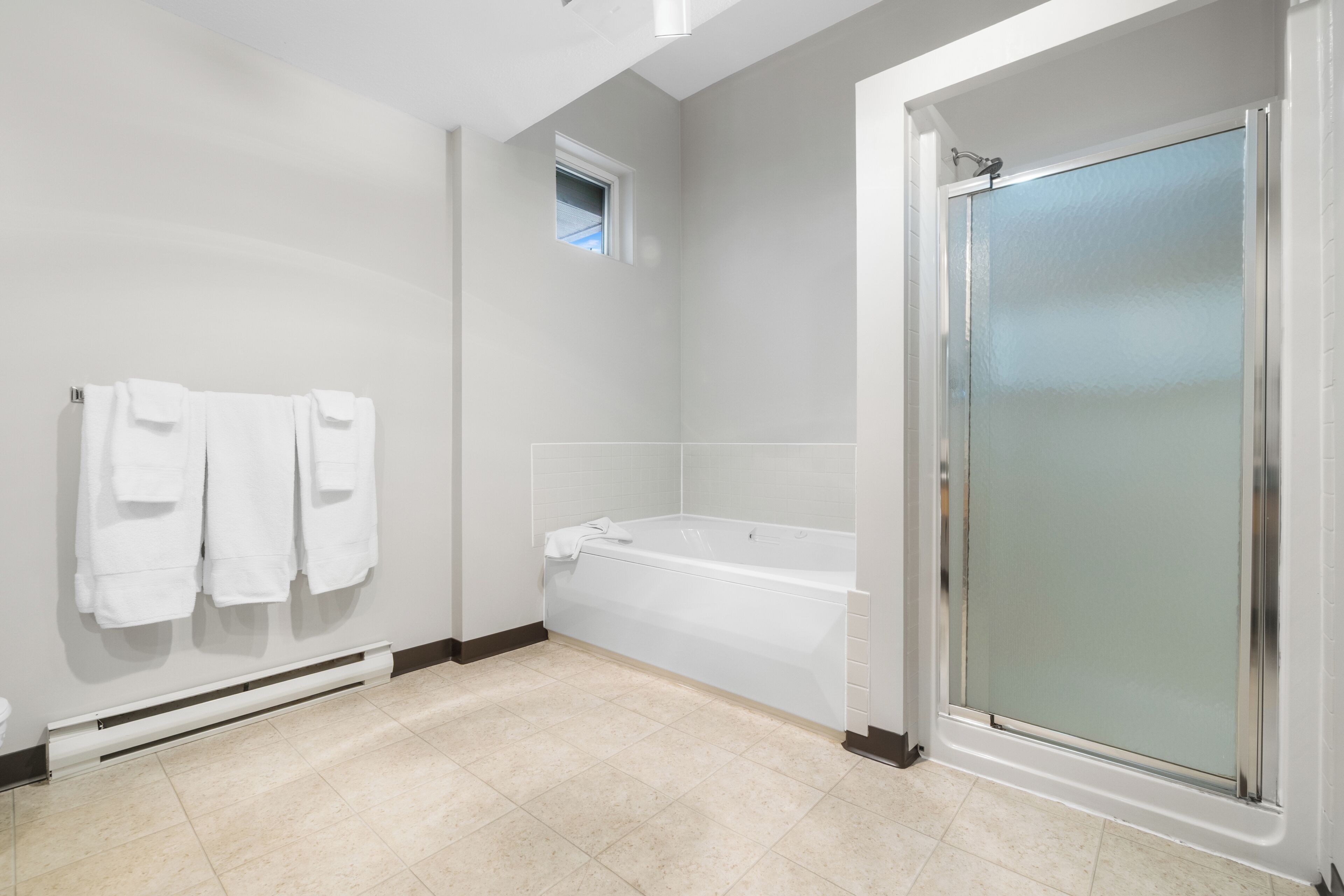A modern bathroom with a bathtub, a glass shower enclosure, and a towel rack with towels.