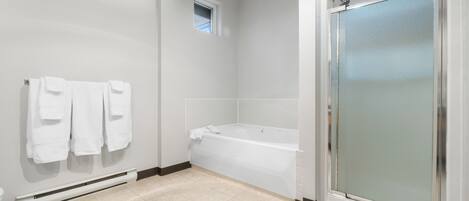 A modern bathroom with a bathtub, a glass shower enclosure, and a towel rack with towels.