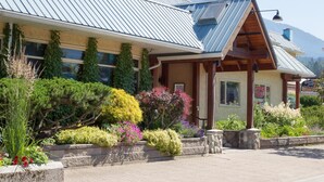 A building with a metal roof, a liquor store sign, and a variety of colorful plants in the front garden. - The Lodge at Arrow Lakes (Nakusp)