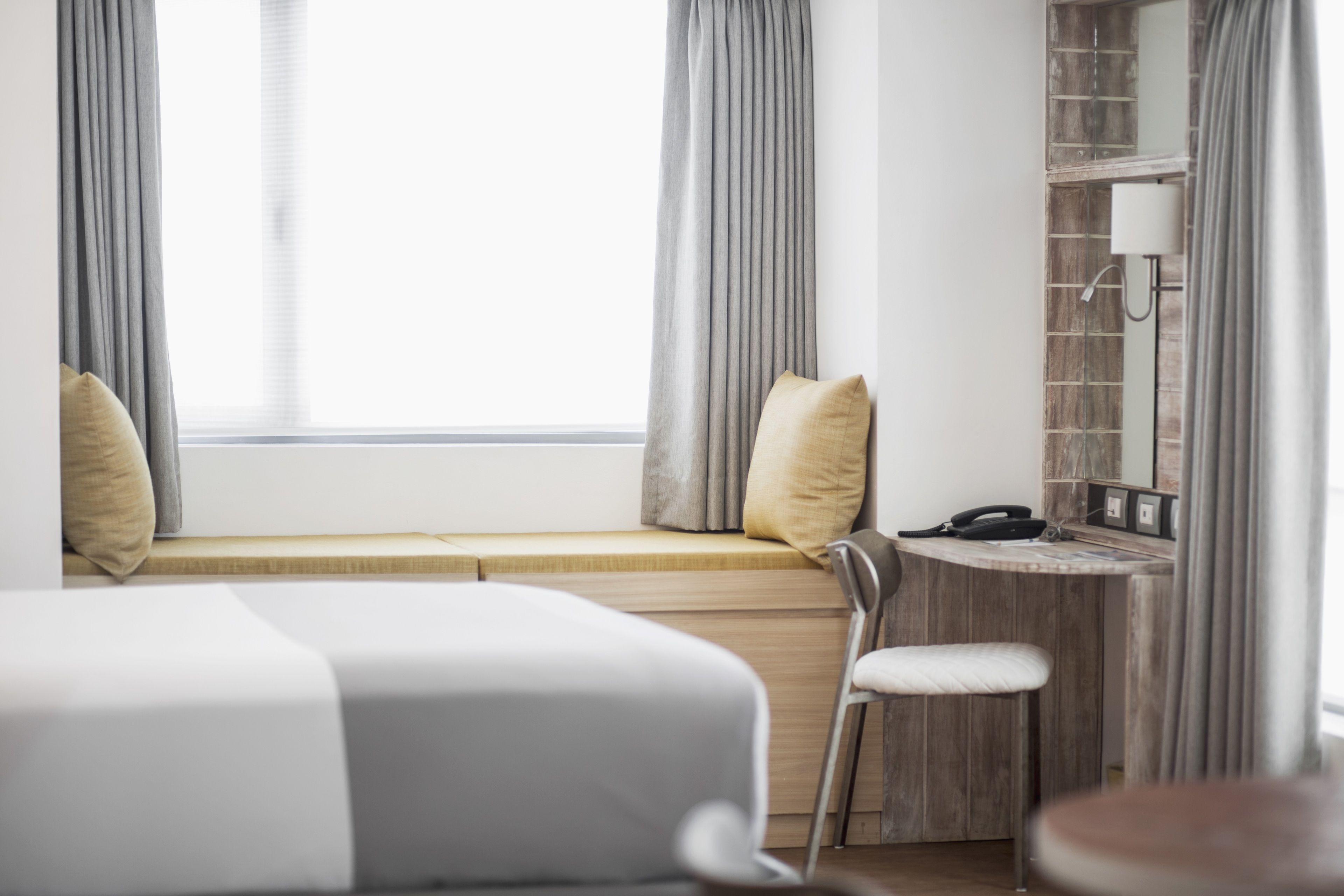 A hotel room with a bed, a desk, a chair, and a window with curtains.