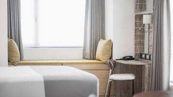 A hotel room with a bed, a desk, a chair, and a window with curtains.
