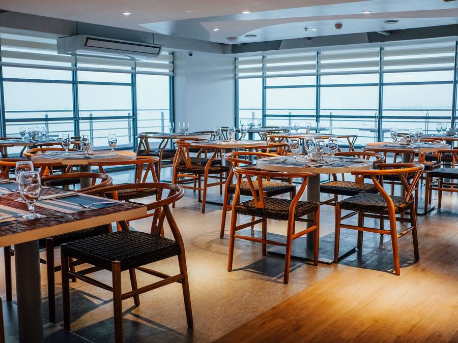 A restaurant with wooden tables and chairs, large windows, and a view of the sky.