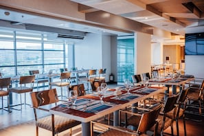 Un espace repas moderne, avec plusieurs tables dressées pour accueillir les clients, de grandes fenêtres offrant une vue sur la ville et un mobilier contemporain.
