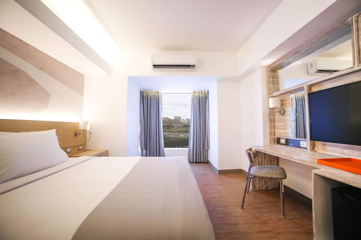 Een hotelkamer met een bed, een bureau met stoel, een grote spiegel en een raam met gordijnen.