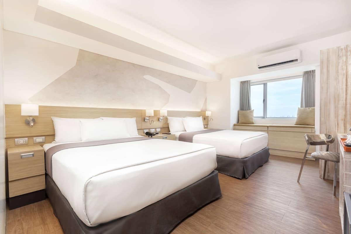 Een hotelkamer met twee bedden, een bureau en een raam met gordijnen.