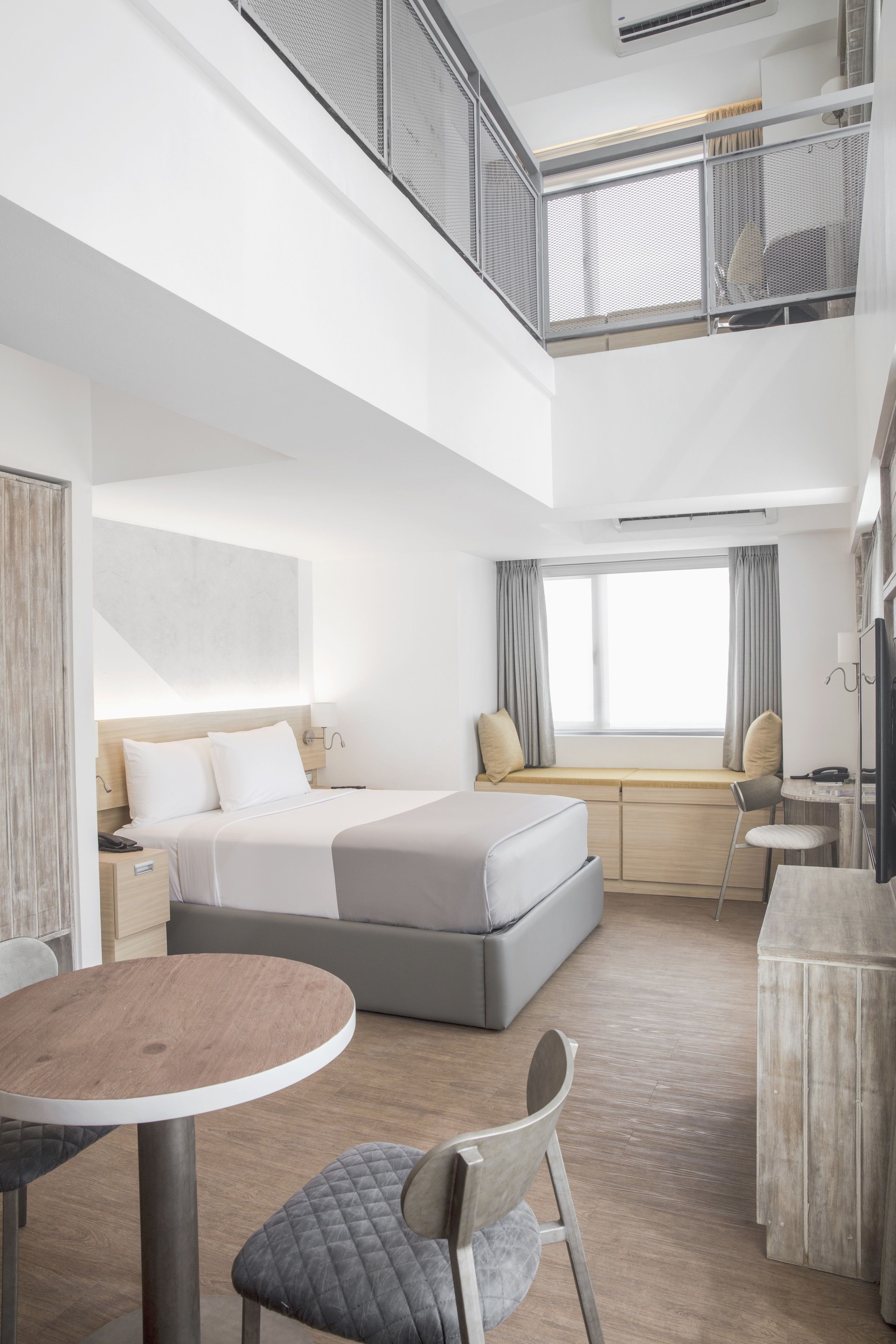 A modern hotel room with a bed, bedside table, and a dining area with a table and chairs.