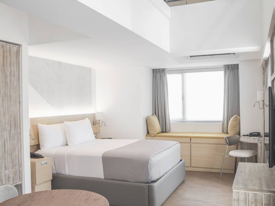 Ein modernes Hotelzimmer mit Bett, Nachttisch und einer Essecke mit Tisch und Stühlen.