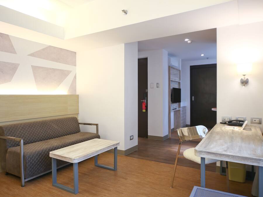 Una habitación de hotel moderna con un sofá, una mesita, una silla y una zona de kitchenette.
