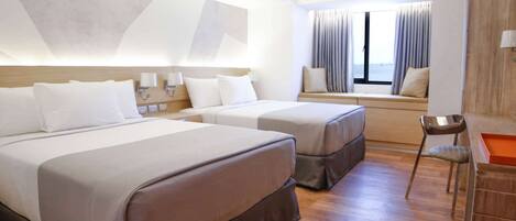 A hotel room with two beds, a window with curtains, an air conditioning unit, and a wooden desk with a chair.