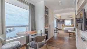 A modern hotel room with a wooden floor, a round dining table with chairs, a sofa, a TV, and a view of the sea. - TRYP by Wyndham Mall of Asia Manila (Pasay)