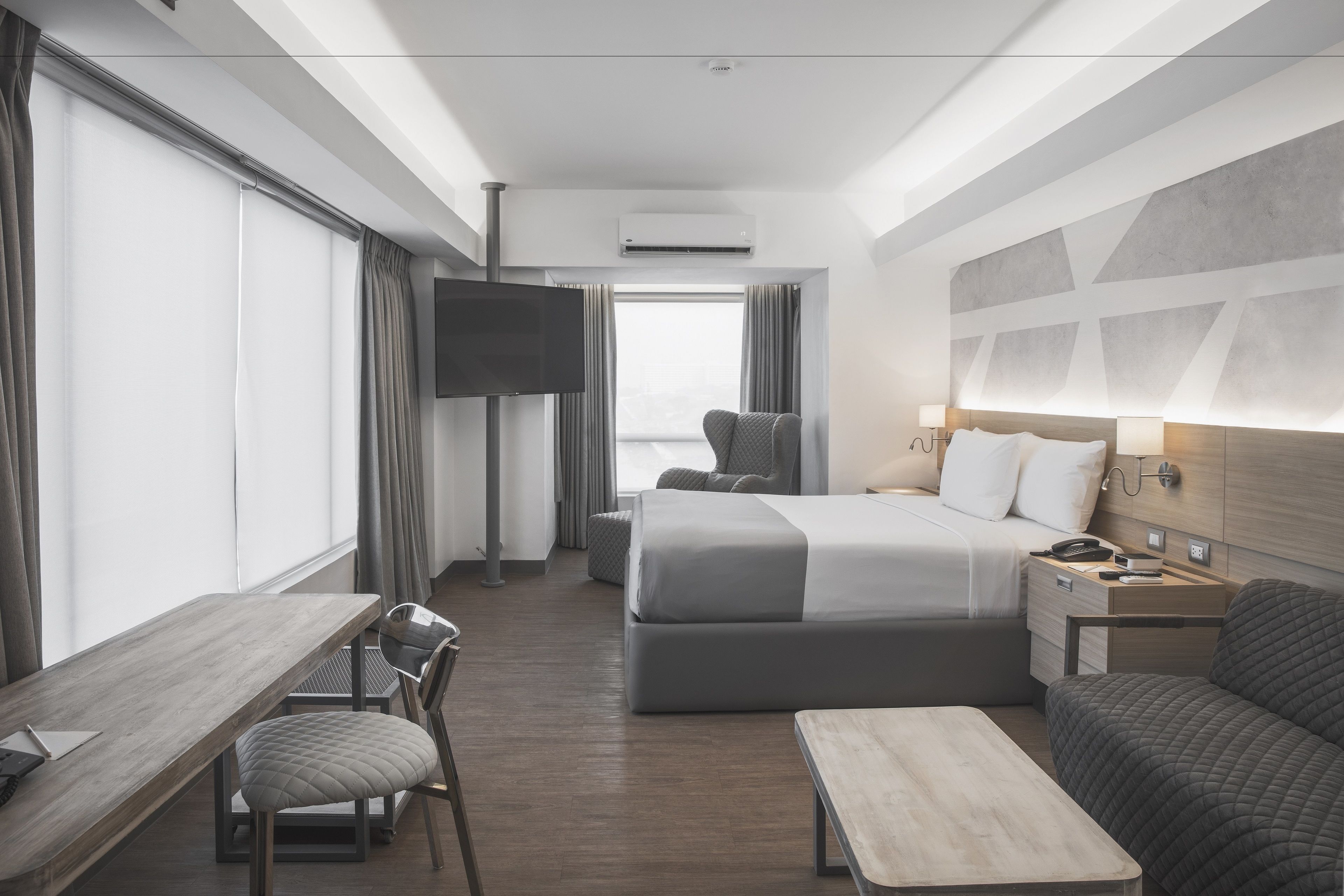 Ein modernes Hotelzimmer mit einem großen Bett, einem Schreibtisch, einem Sessel, einer Couch und einem Fernseher.