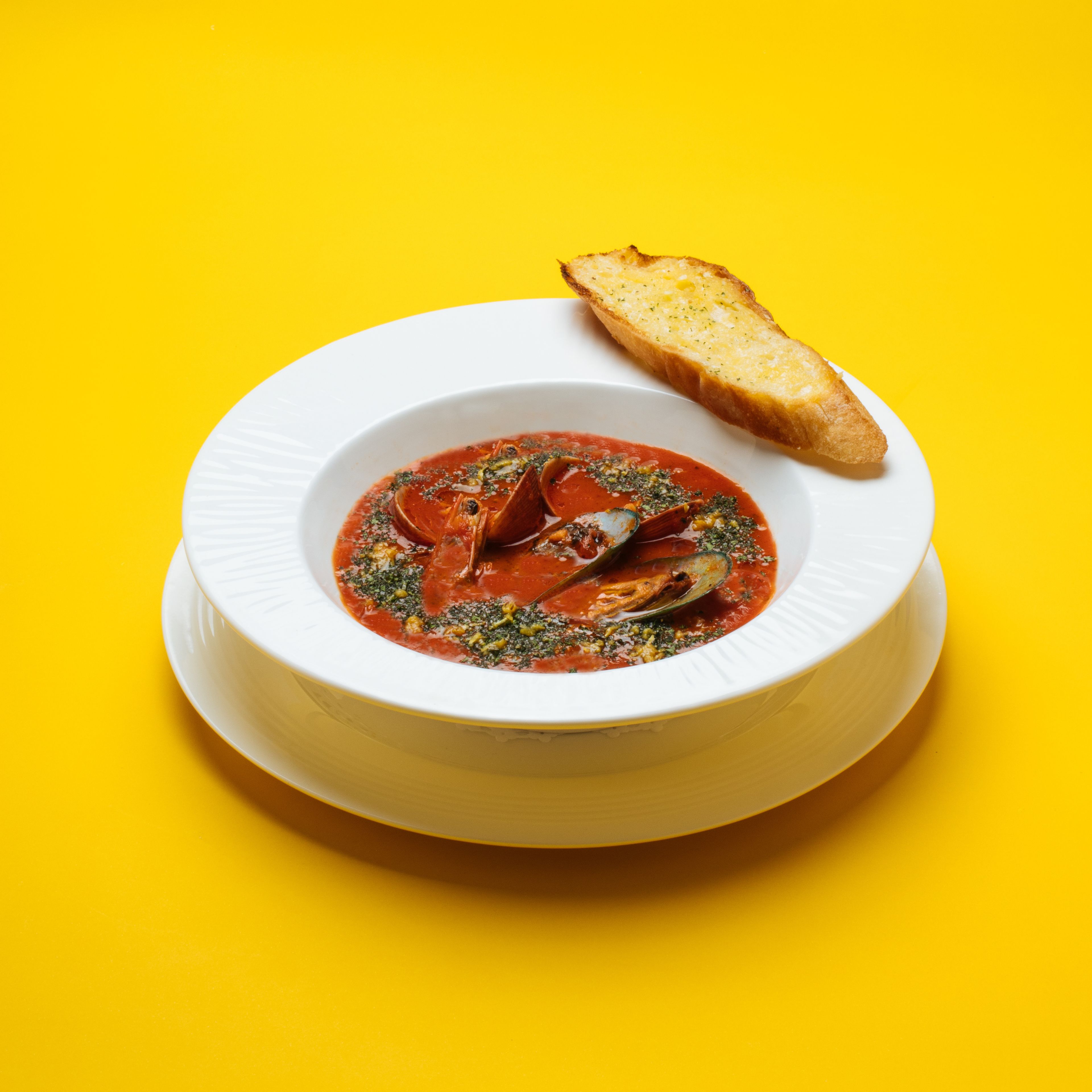 Un tazón blanco de sopa con mejillones y hierbas sobre un fondo amarillo.