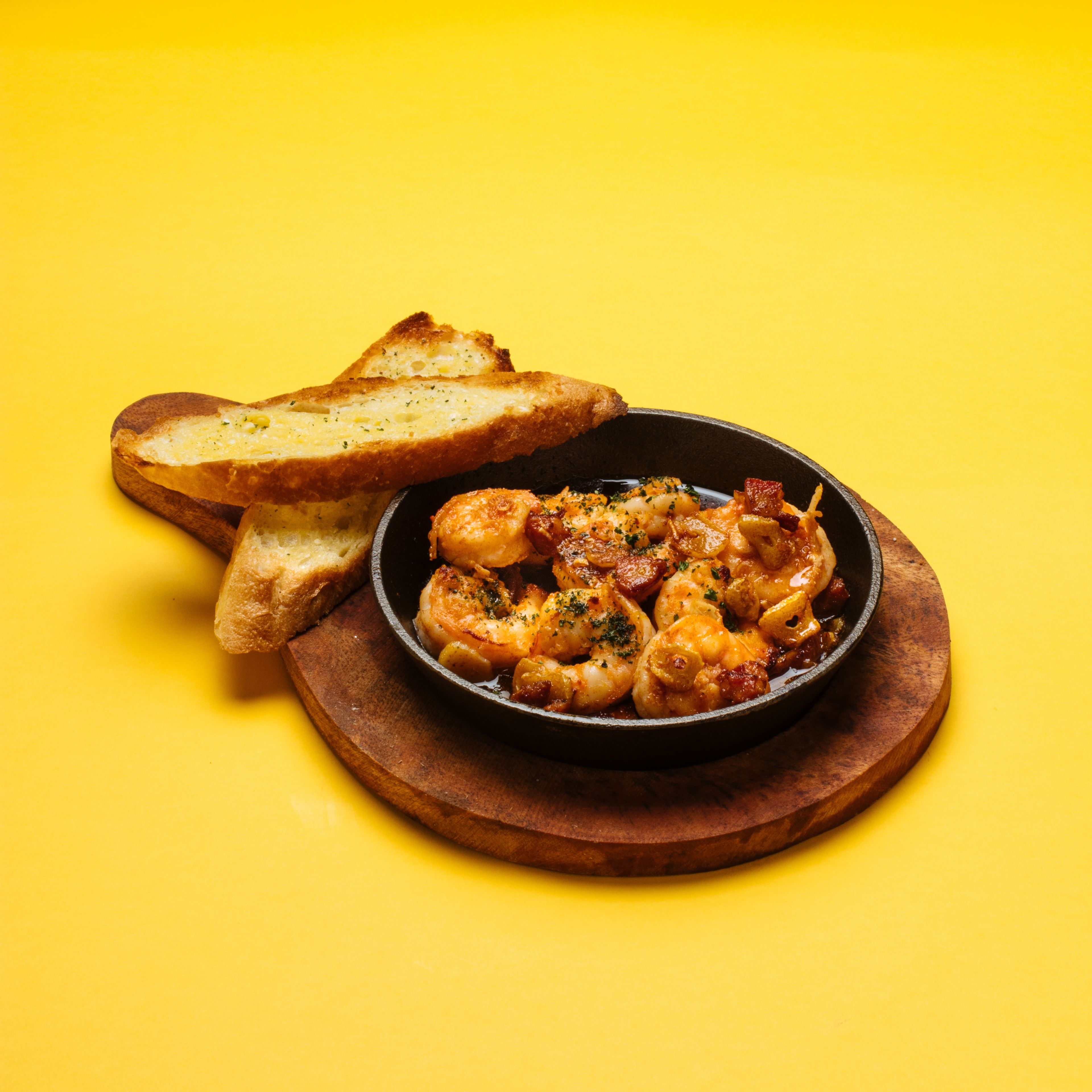 A dish of shrimp in a skillet with toasted bread on a wooden board.