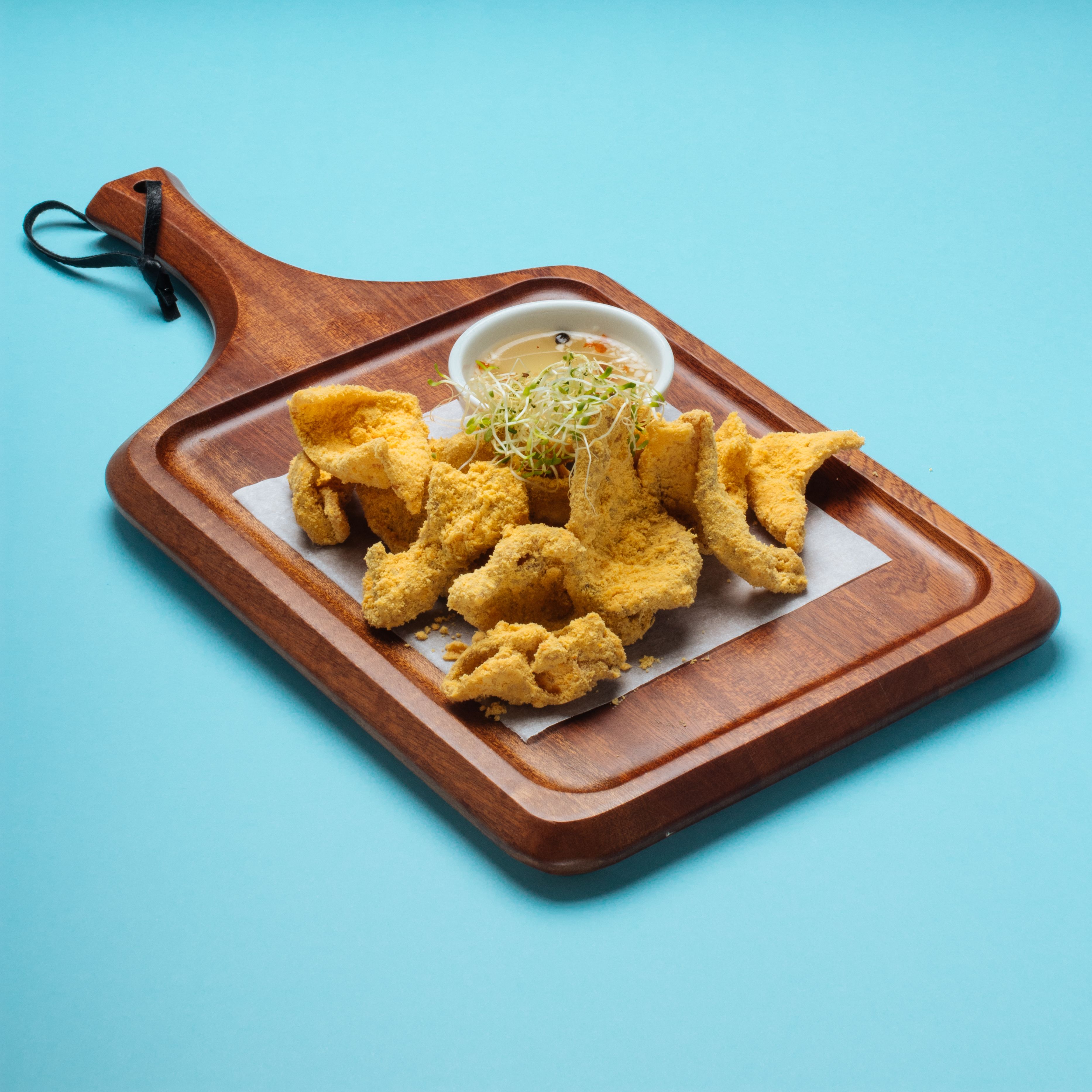A wooden tray with fried food and a small bowl of dipping sauce.