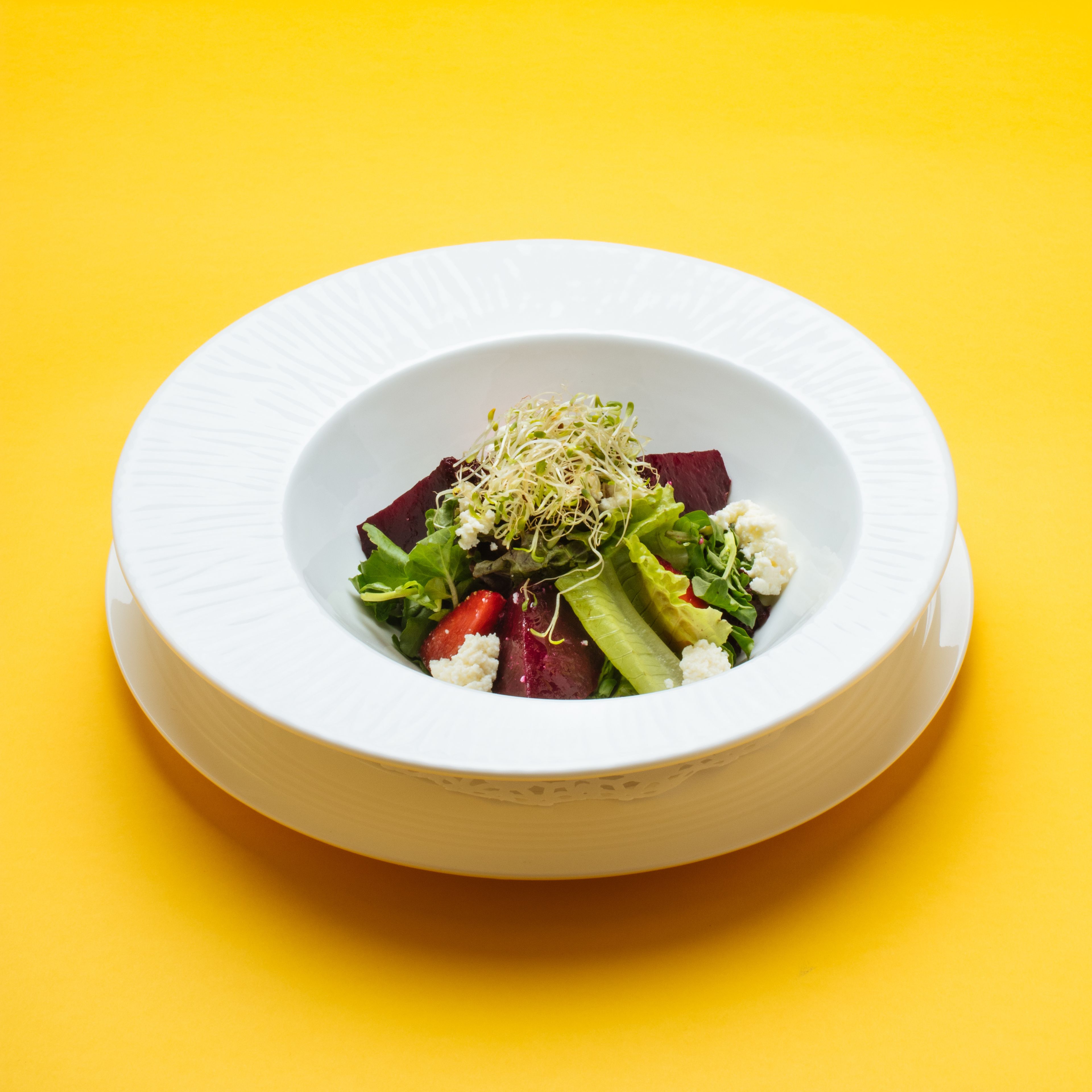 Une assiette blanche avec une salade, le tout sur un fond jaune.