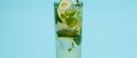 A tall glass with a lime slice and mint leaves filled with a clear liquid, set against a light blue background.