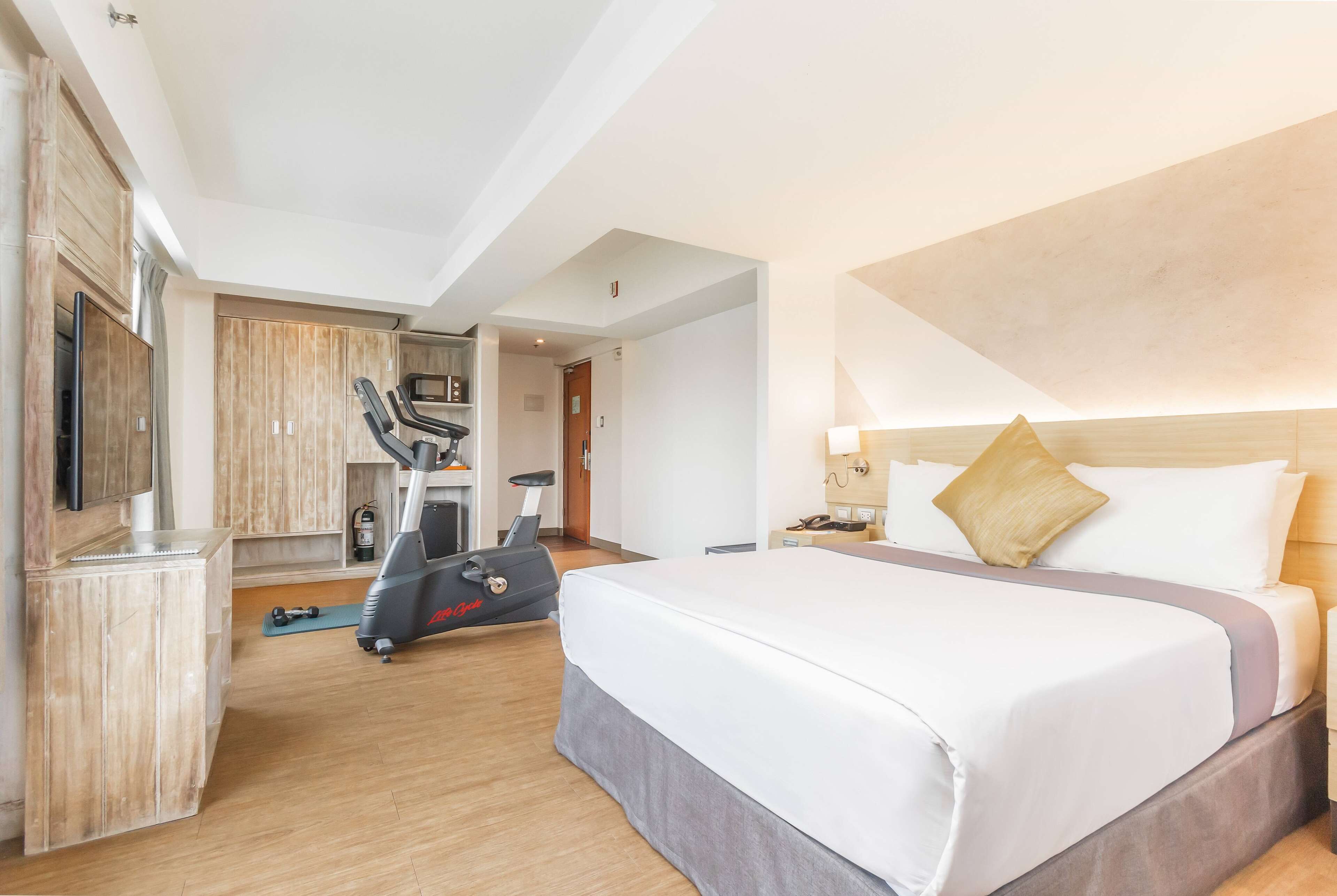 Una habitación de hotel con cama, equipo de ejercicio, televisor y minibar.