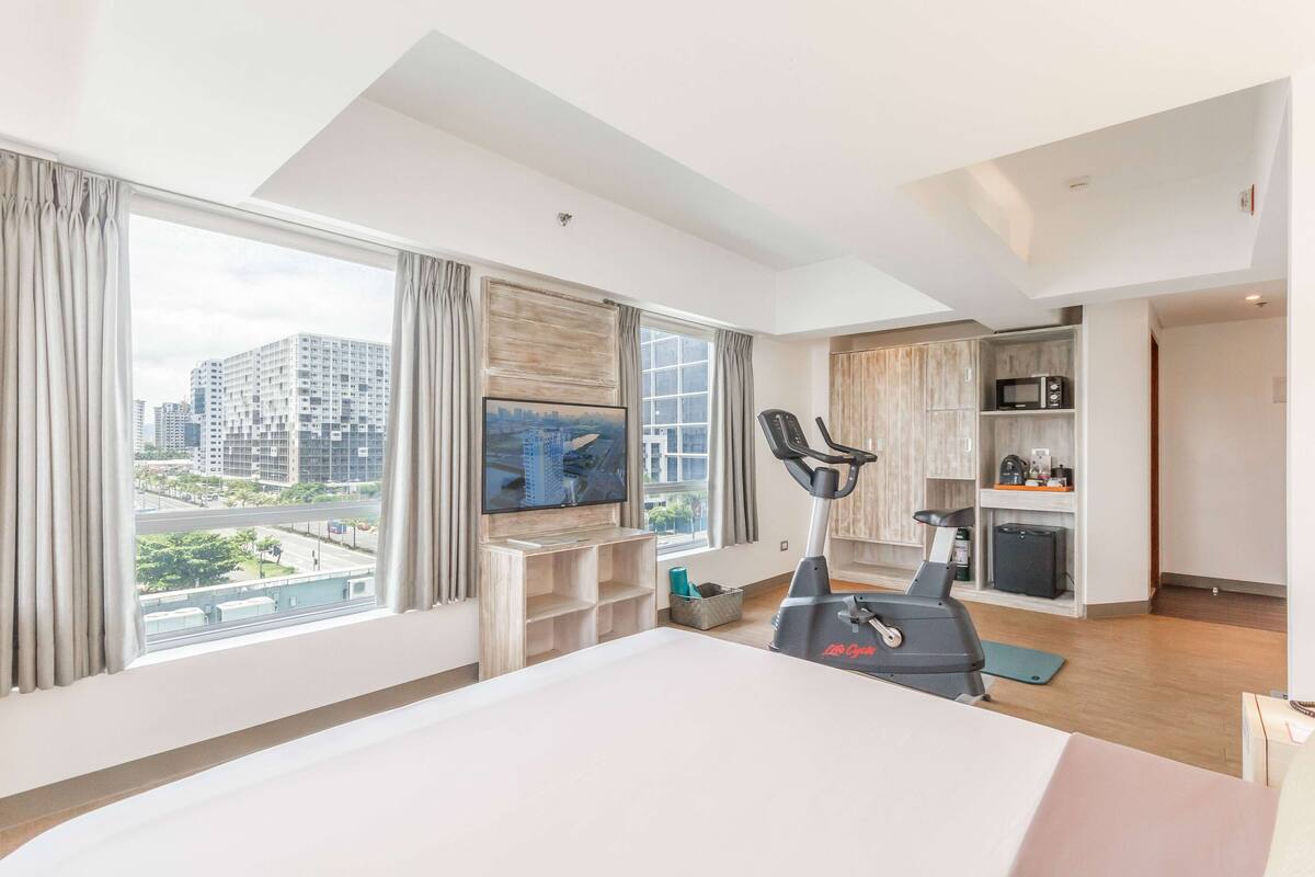 Een moderne hotelkamer met een groot bed, een televisie, een loopband en uitzicht over de stad.