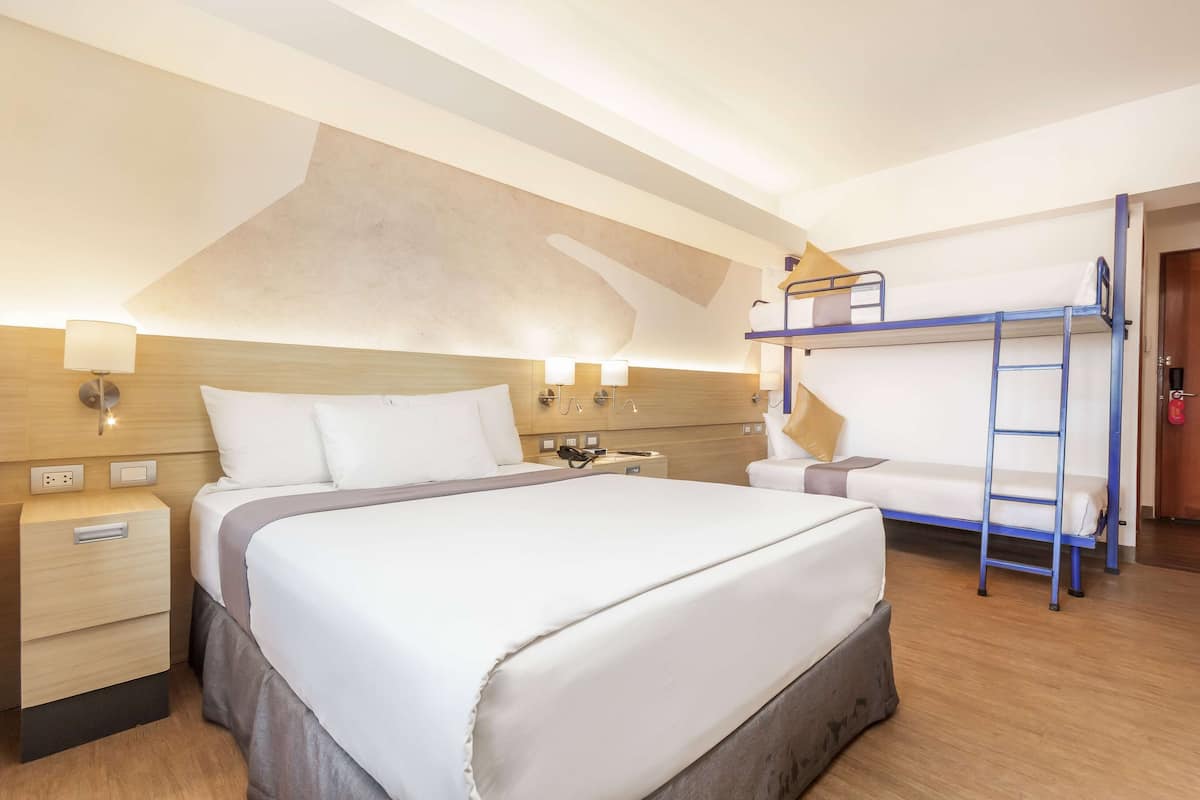 Een hotelkamer met een groot bed, een nachtkastje met een lamp, een stapelbed en een houten hoofdbord.