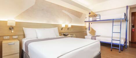 A hotel room with a large bed, a bedside table with a lamp, a bunk bed, and a wooden headboard.