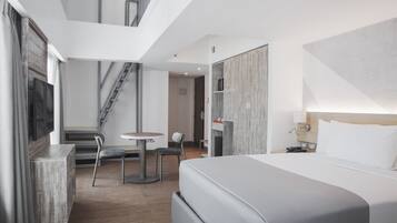 A modern hotel room with a large bed, a desk, and a chair. There is a staircase leading to an upper level.