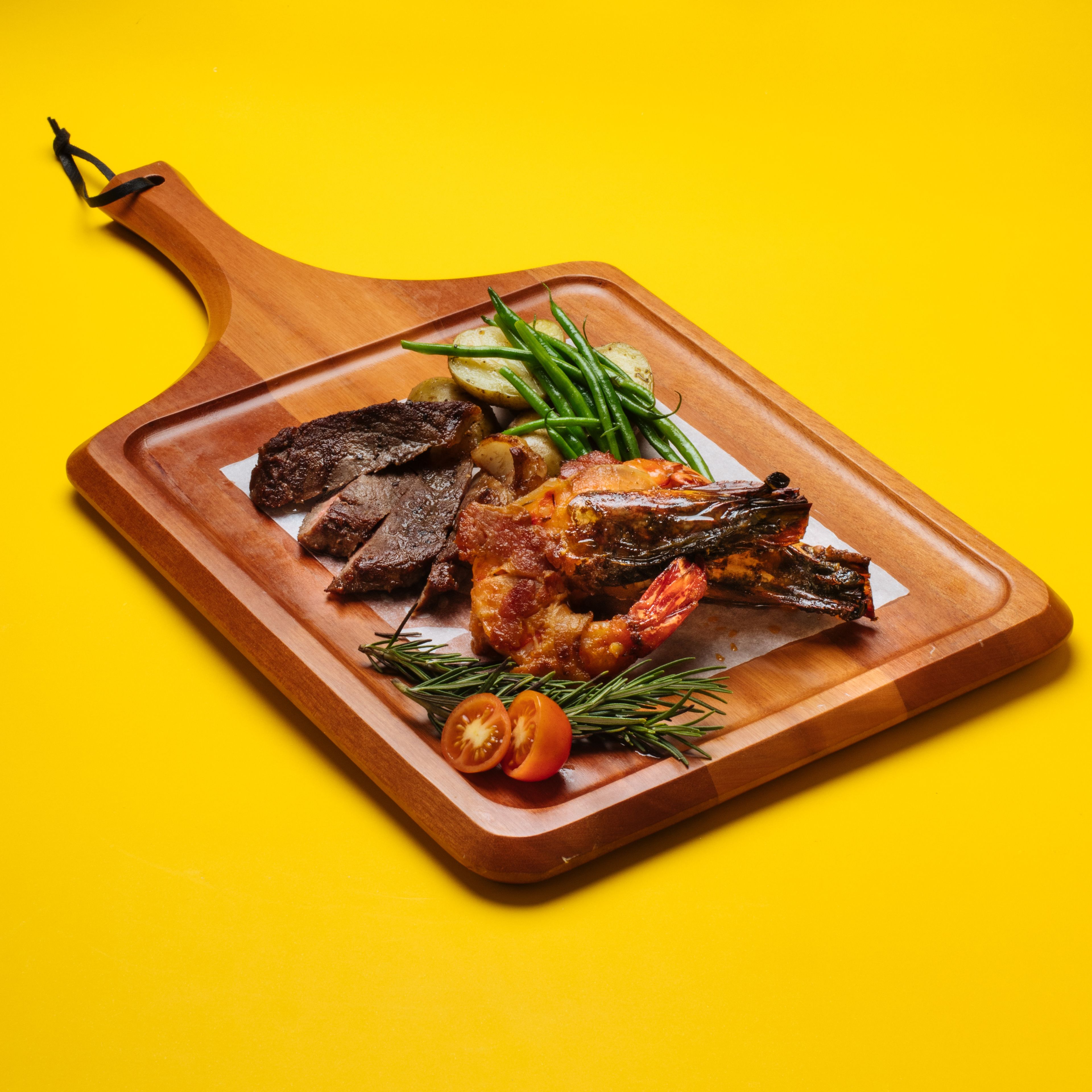 A wooden serving board with various meats and vegetables.